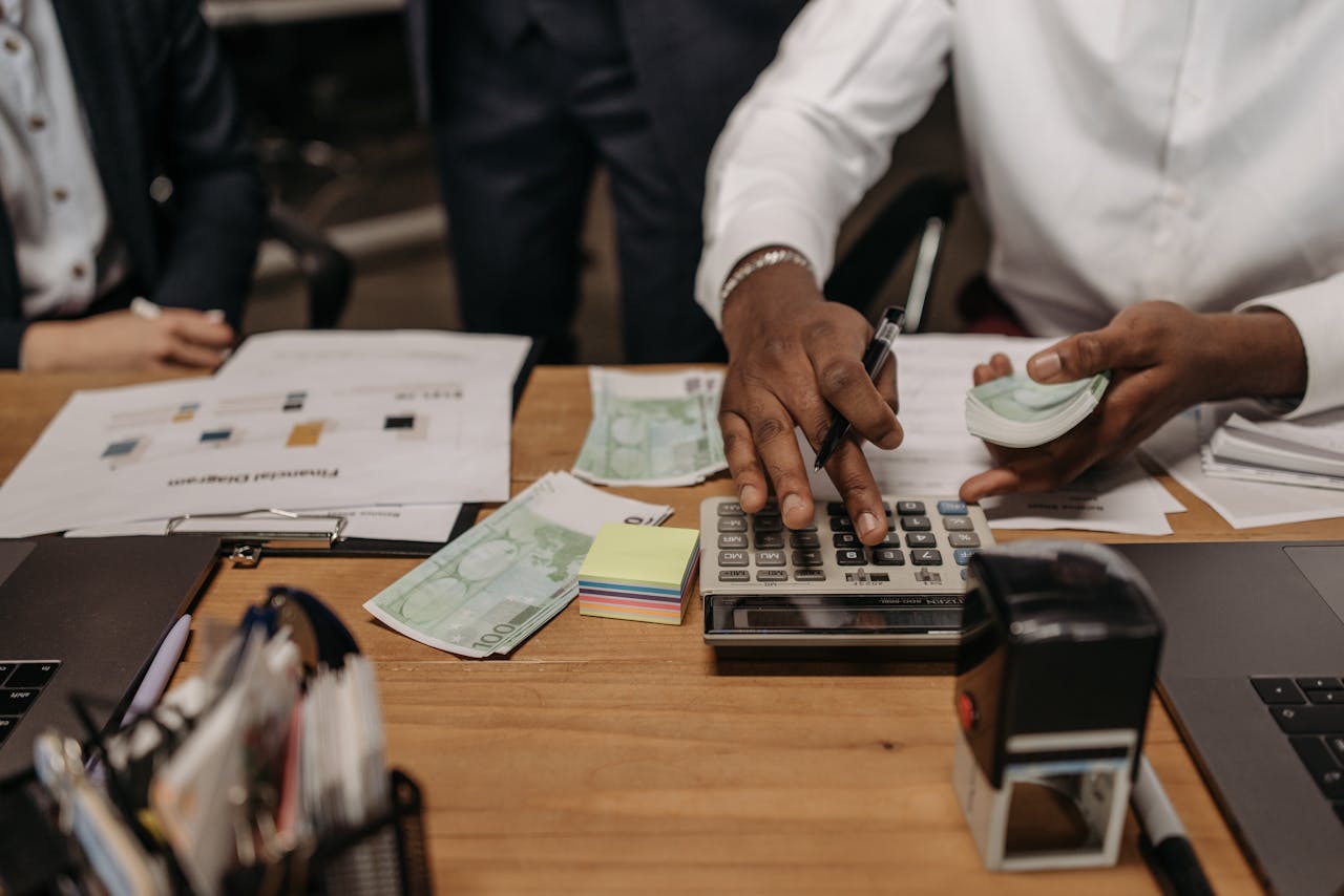 Professional setting with people handling cash and calculations using a calculator at a desk.