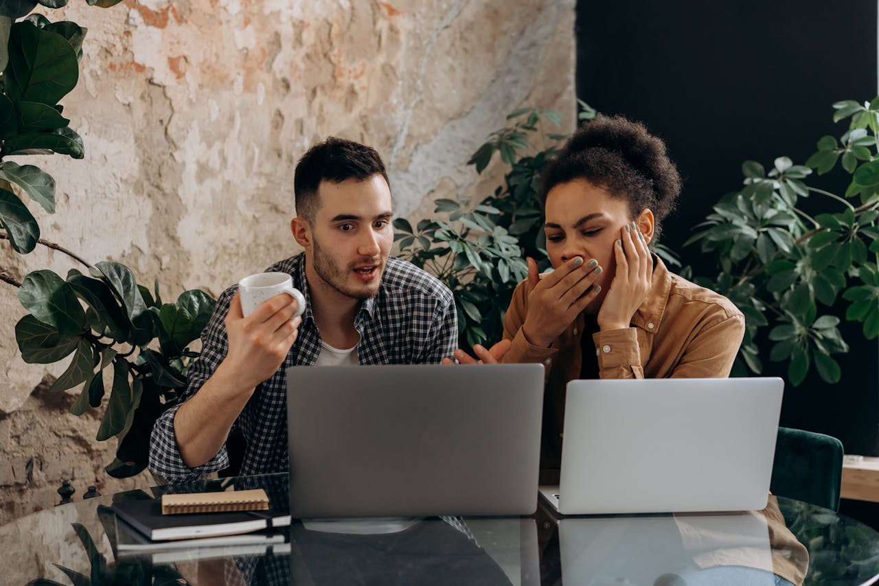 Two young adults working together on laptops in a cozy home office setting.