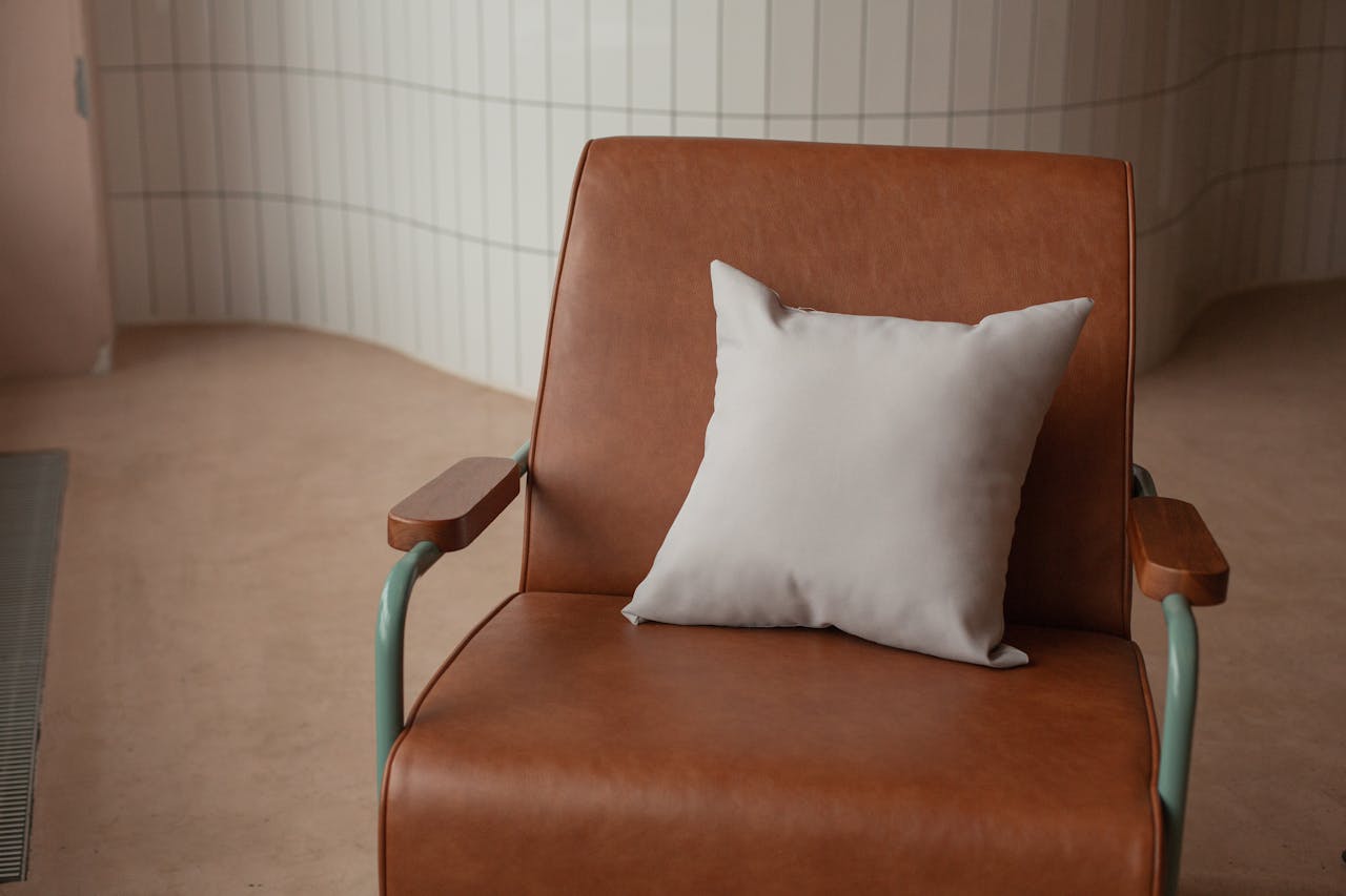 A stylish brown leather chair with a light cushion in a modern indoor setting, showcasing minimalistic design.